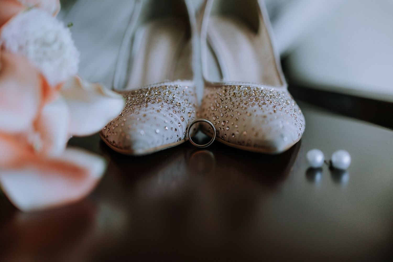 Close-up of sparkly bridal shoes with wedding rings in soft focus.