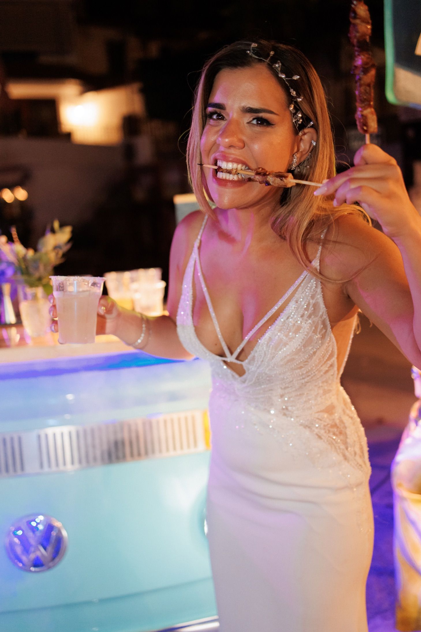 An elegant white wedding dress shown in an evening party setting with blue lighting.