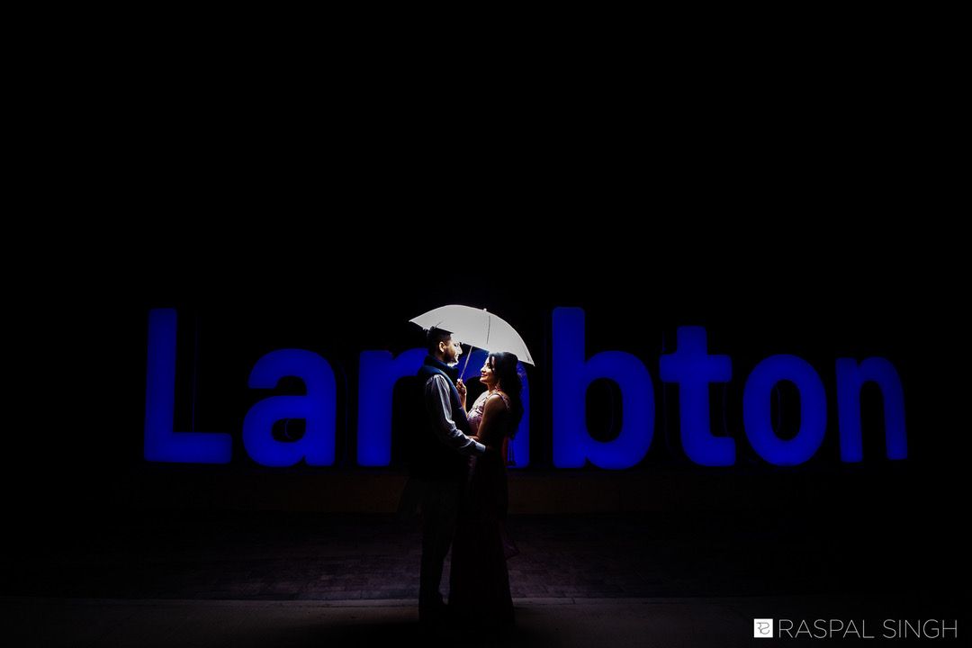 A silhouetted couple stands under an umbrella against a dark background with blue Lambton text.