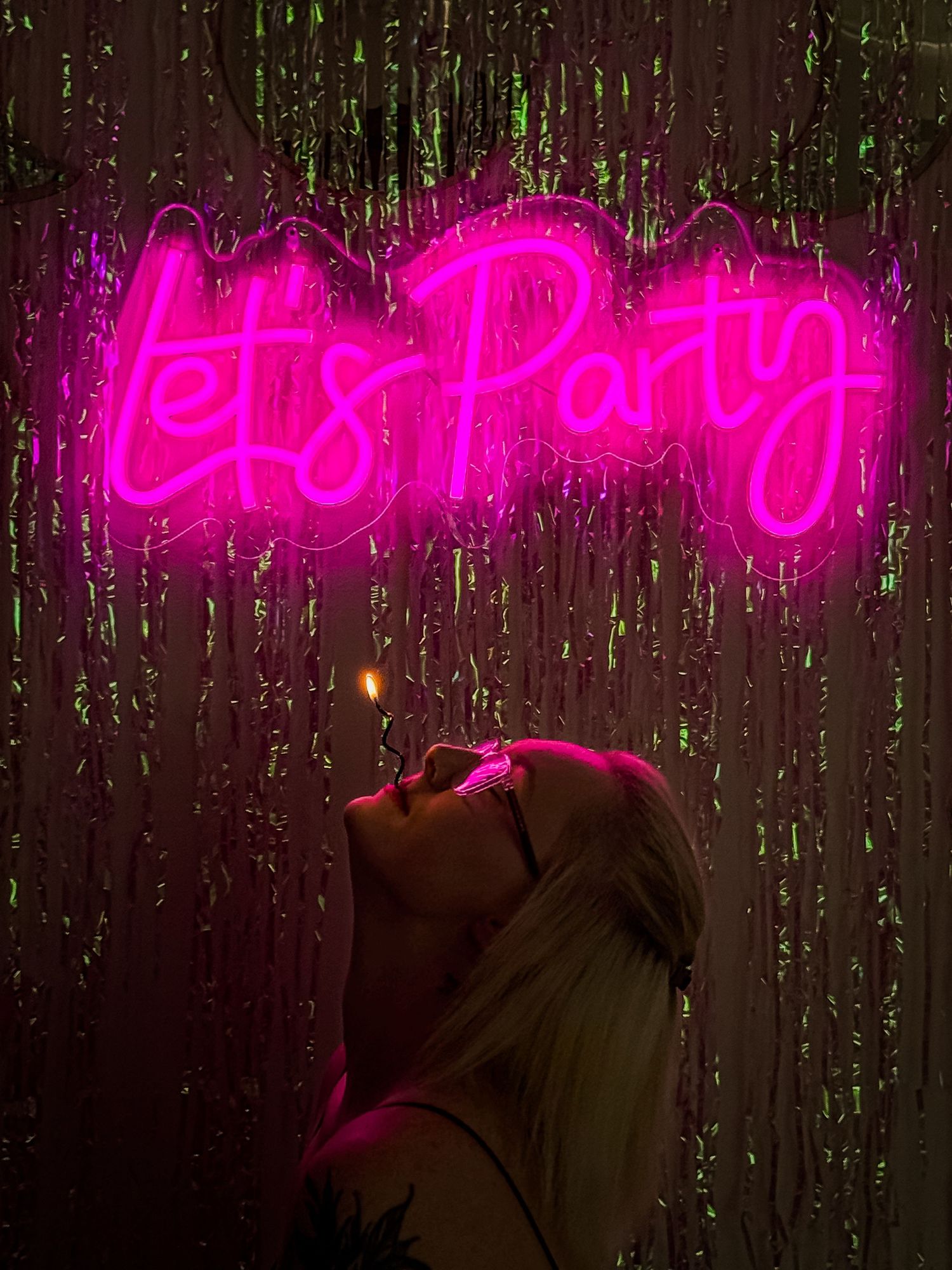 Neon pink text signs glowing against dark background with sparkly tinsel decorations.