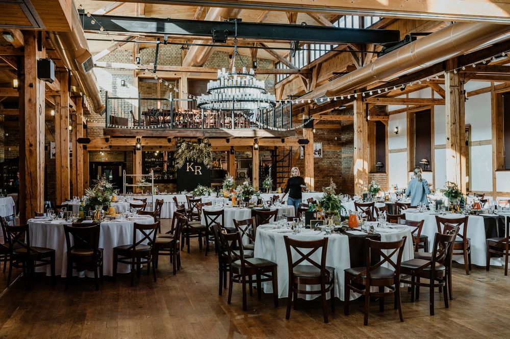 Rustic wedding reception venue with wooden beams, chandeliers and round tables.