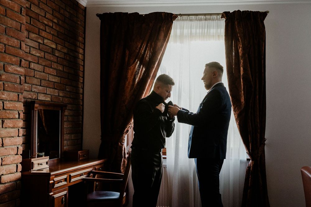 Silhouettes against window light in brick-walled room during wedding preparations.