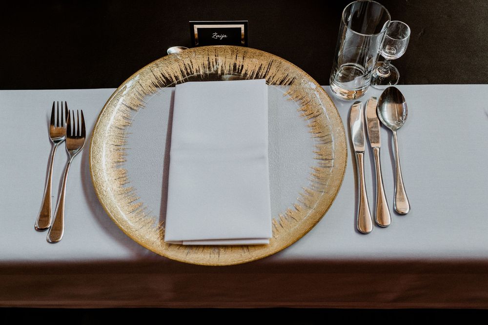 Formal place setting with gold rimmed charger plate and elegant silverware arrangement.