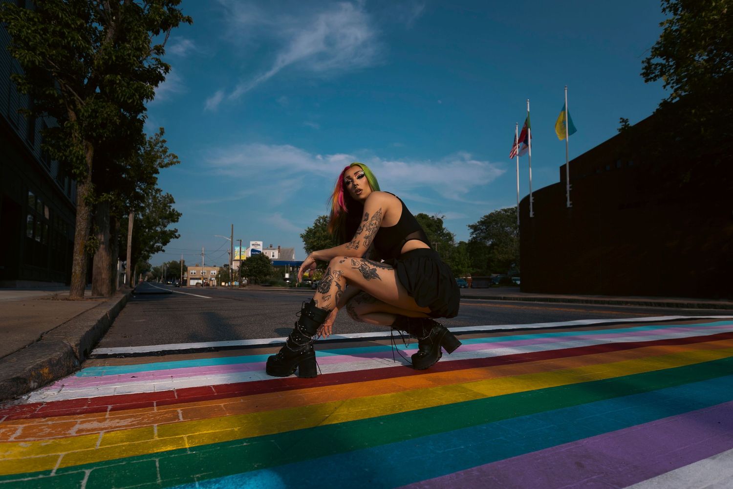 A person strikes various dance poses on a colorful rainbow crosswalk under a bright blue sky.