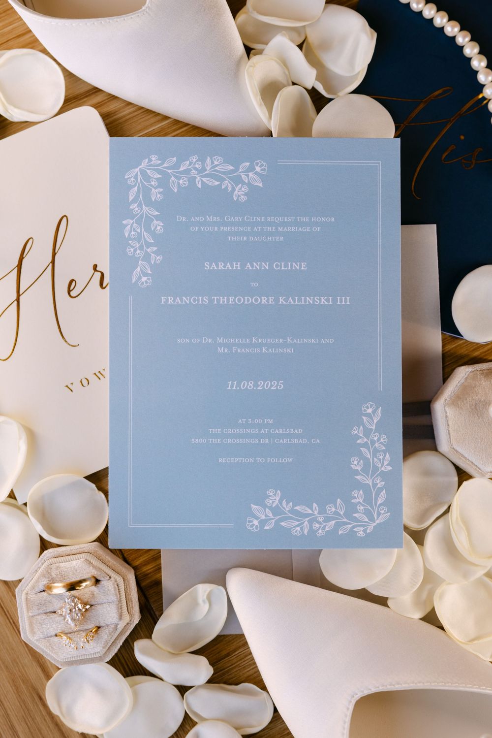 Elegant light blue wedding invitation with floral details surrounded by white petals and accessories.