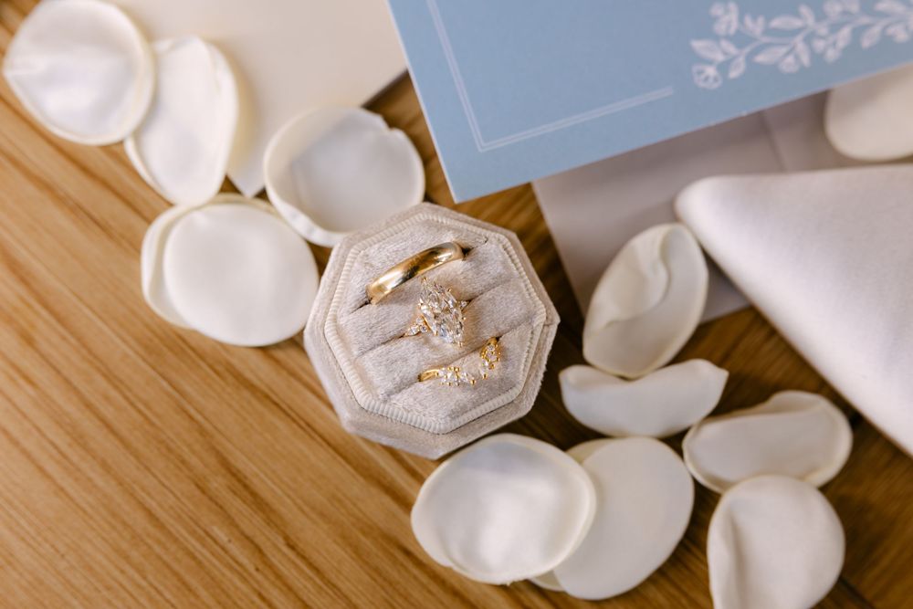 Wedding rings and white rose petals arranged on a wooden surface with a light blue box.