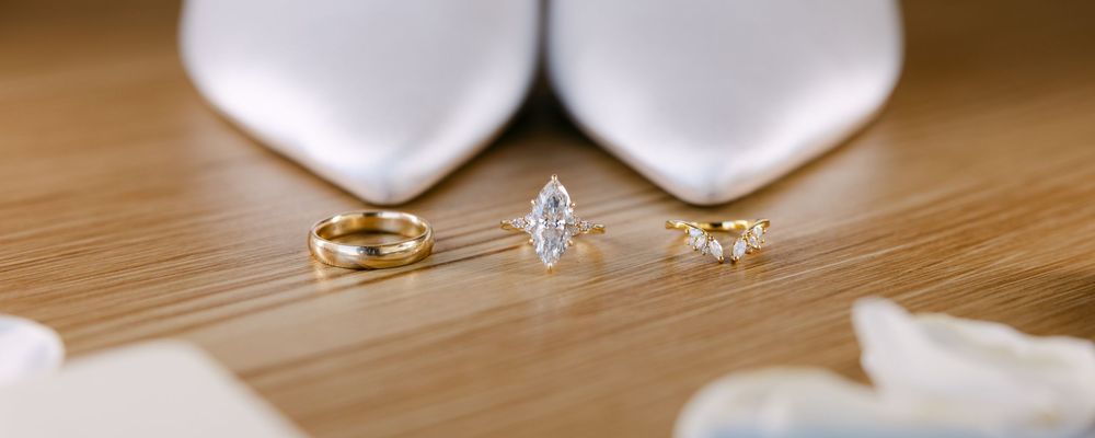 Wedding rings and white heels arranged on a wooden surface in elegant composition.