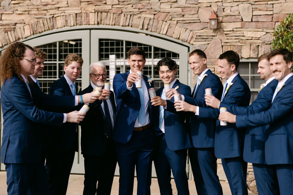 Groomsmen in navy suits lined up against stone wall for formal wedding photo.