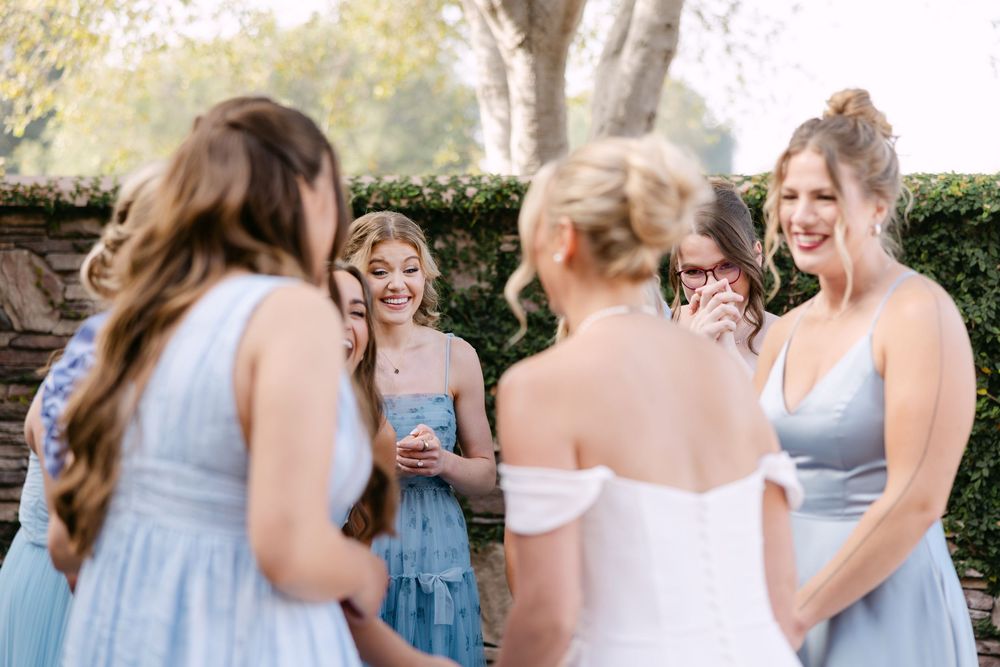Bridesmaids in light blue dresses laugh and celebrate outdoors during a wedding event.