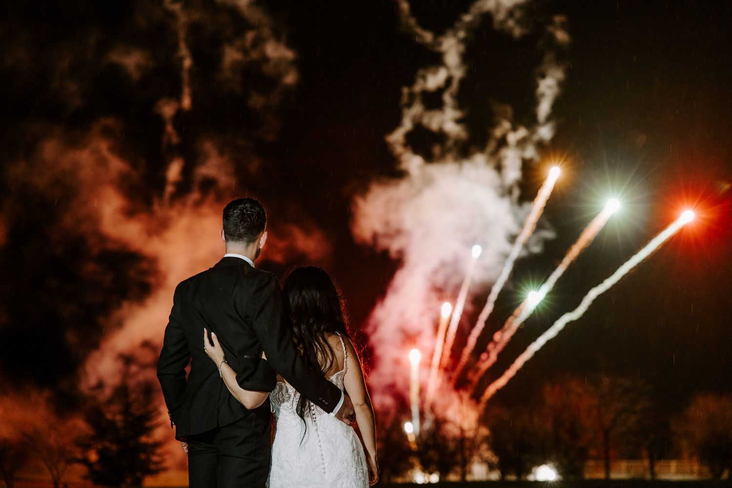 Silhouettes of a couple embrace against a dark sky illuminated by colorful fireworks during a romantic celebration.