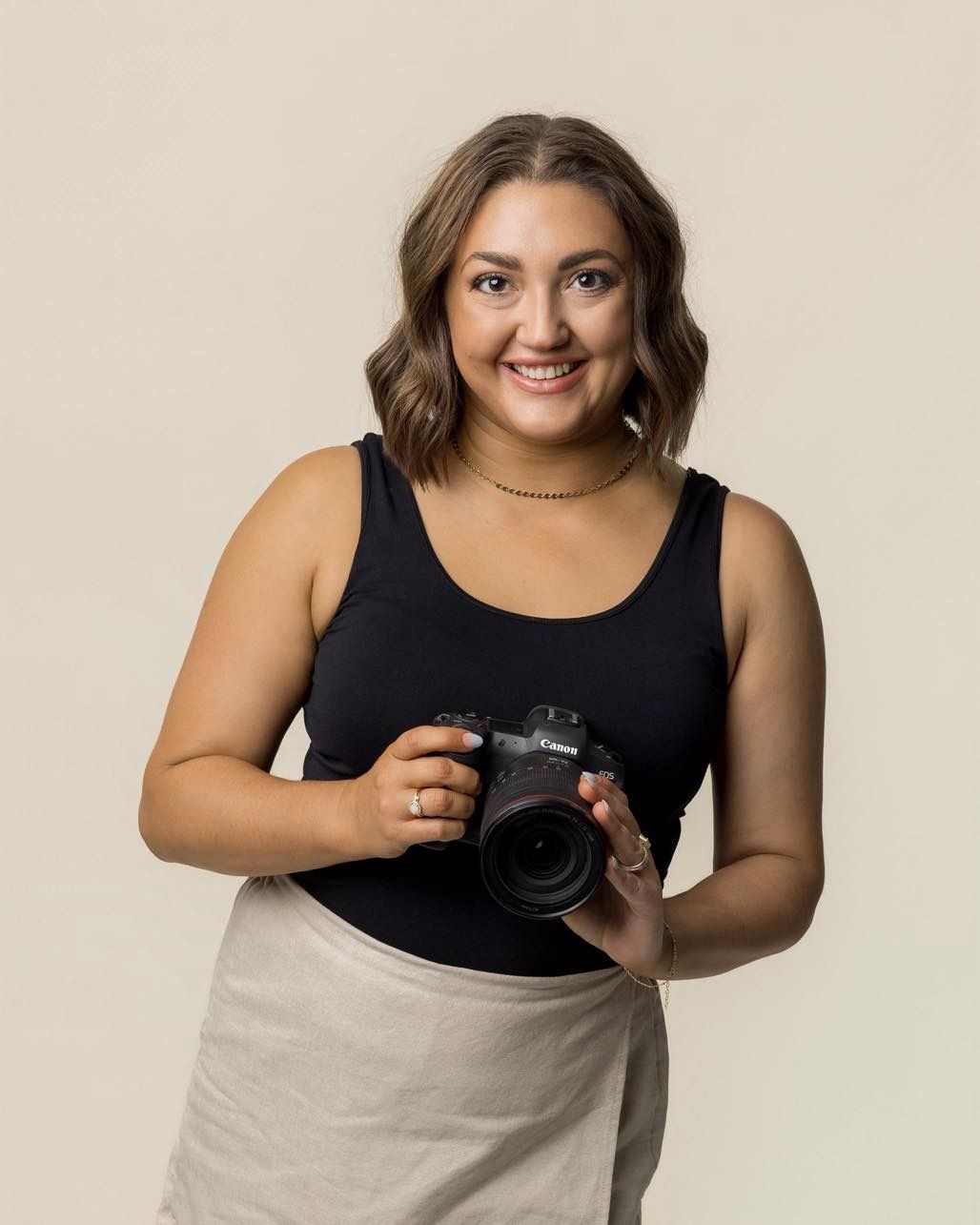 Person holding professional camera while posing against light background.