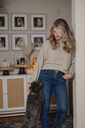 Person playing with small black dog in cozy living room with framed photos.