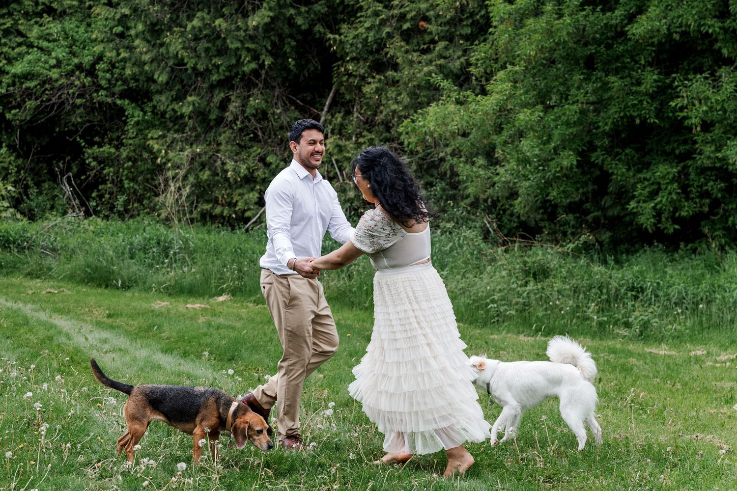 A couple and their dogs enjoy a playful moment together in a lush green field during an outdoor photo session.
