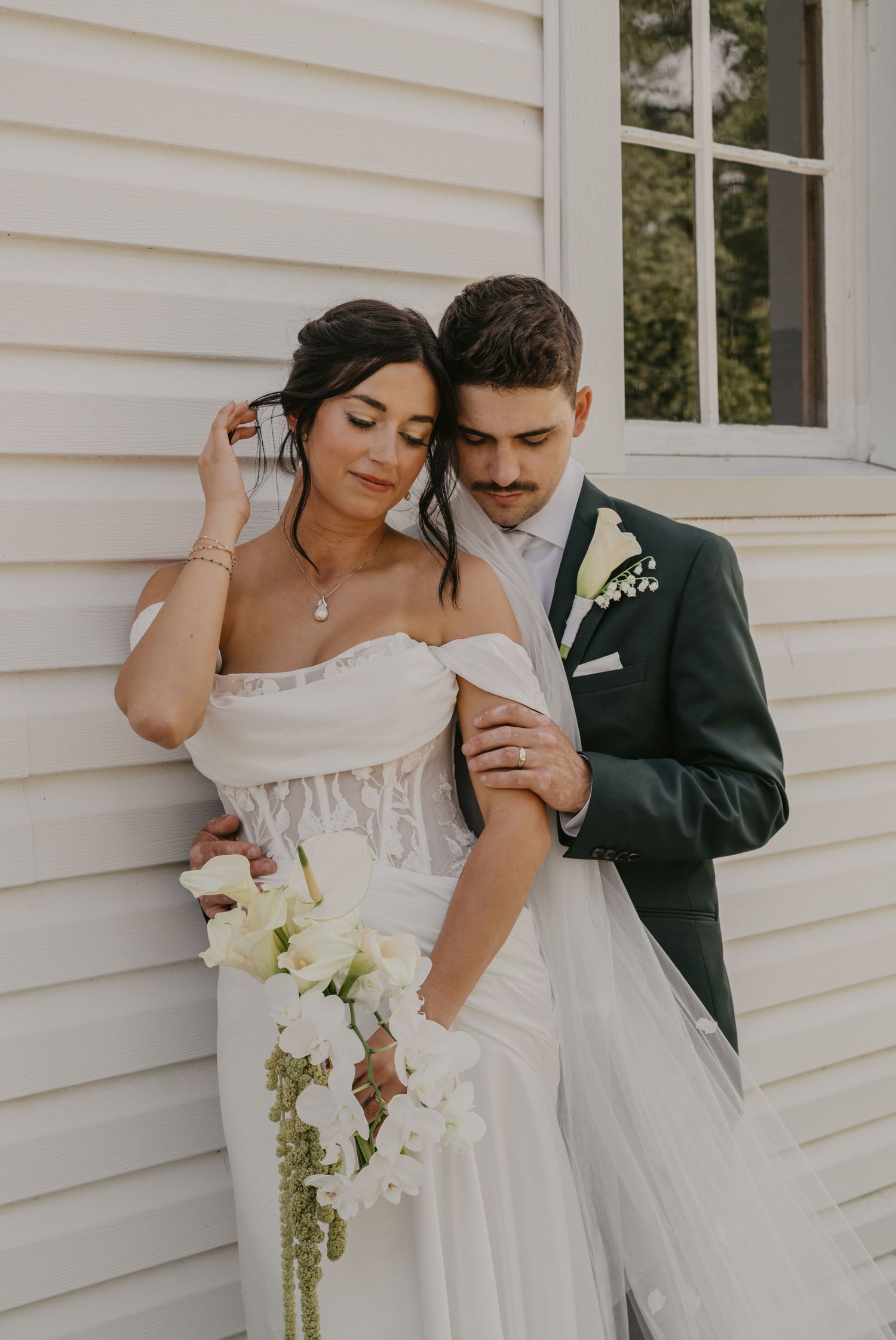 A romantic wedding couple embraces in front of a white clapboard wall in a series of intimate poses.