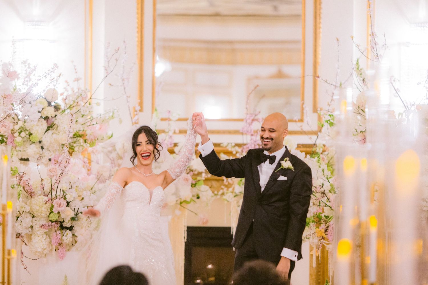 A couple shares a romantic dance moment at an elegant wedding reception decorated with pink and white floral arrangements.