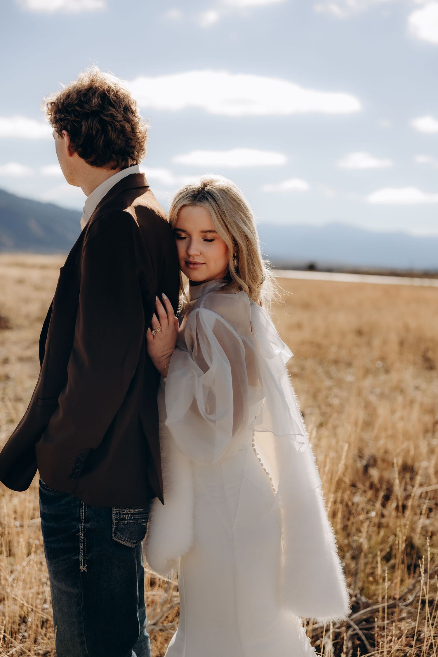A couple shares an intimate moment in a golden wheat field under cloudy skies during a wedding photoshoot.