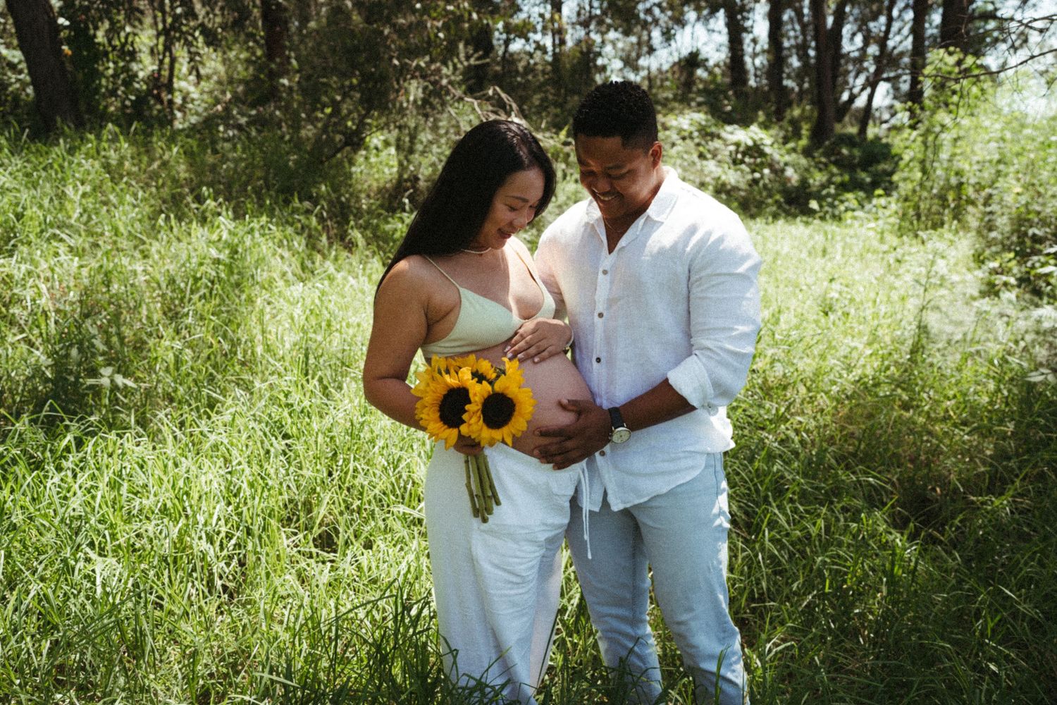 A couple in white outfits enjoying a sunny day among trees and sunflowers.