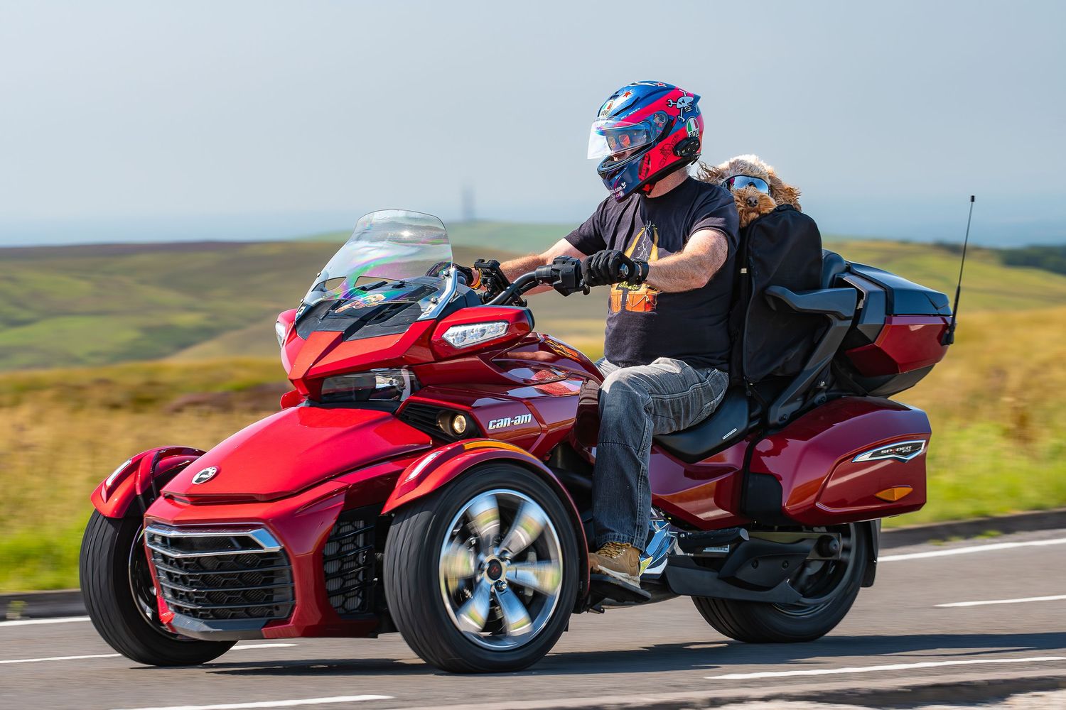 A rider on a red Can-Am Spyder three-wheel motorcycle cruises along a scenic mountain road.