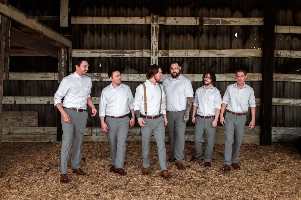 Wedding party members arrange themselves playfully along wooden barn beams.