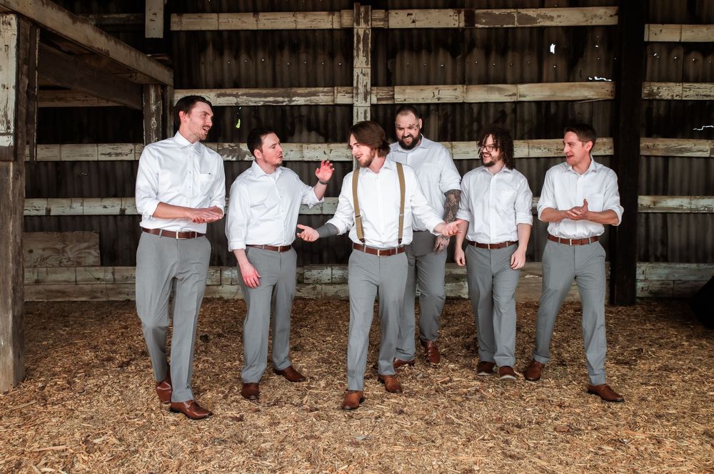 Two people in white shirts and gray pants stand together against weathered wooden barn walls.