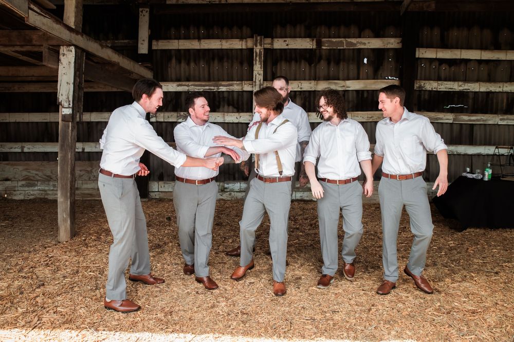 Two people in matching suspenders and dress shirts pose casually in a rustic barn interior.
