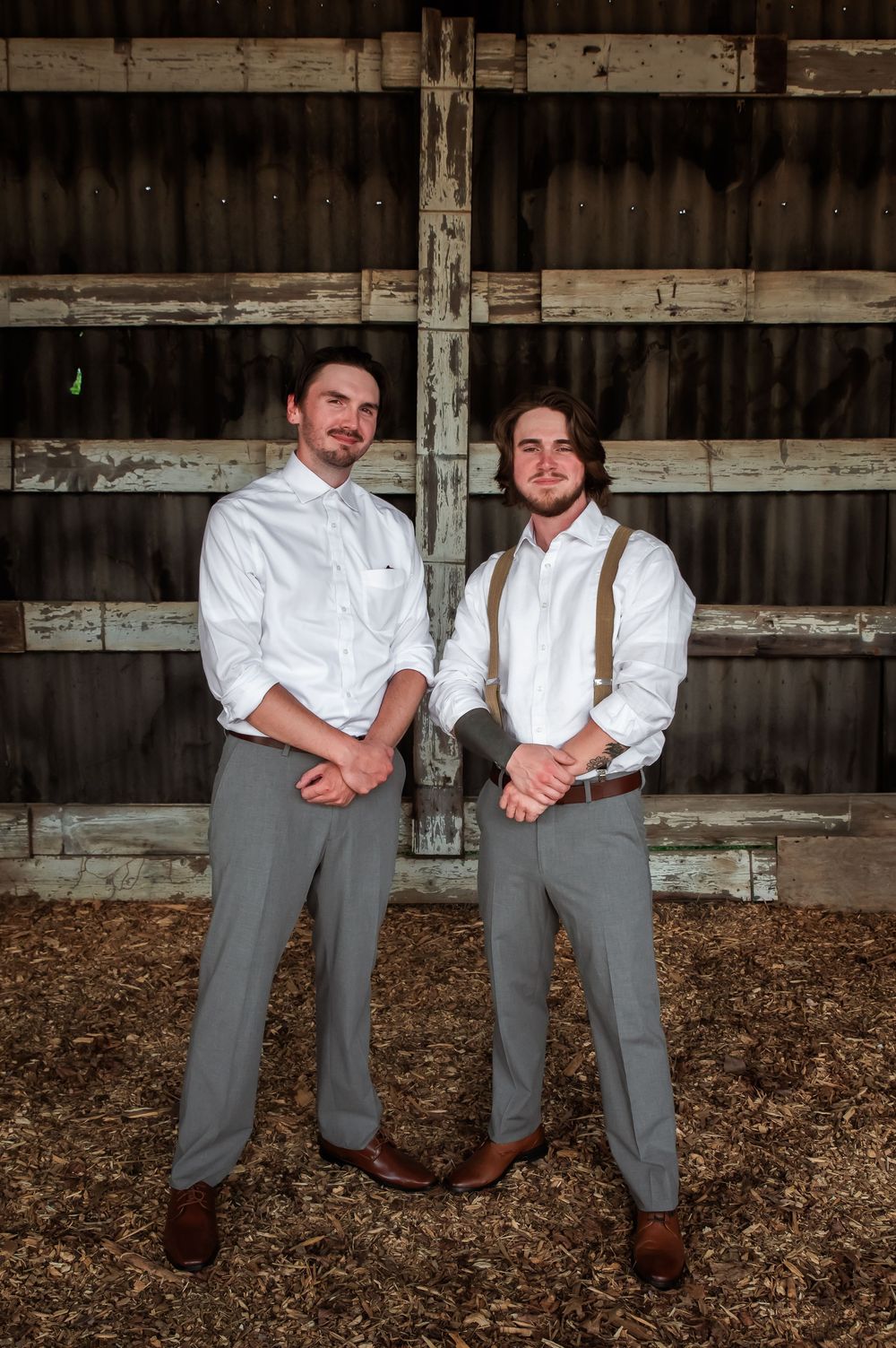 Two people in matching gray pants and white shirts pose together in rustic barn setting.