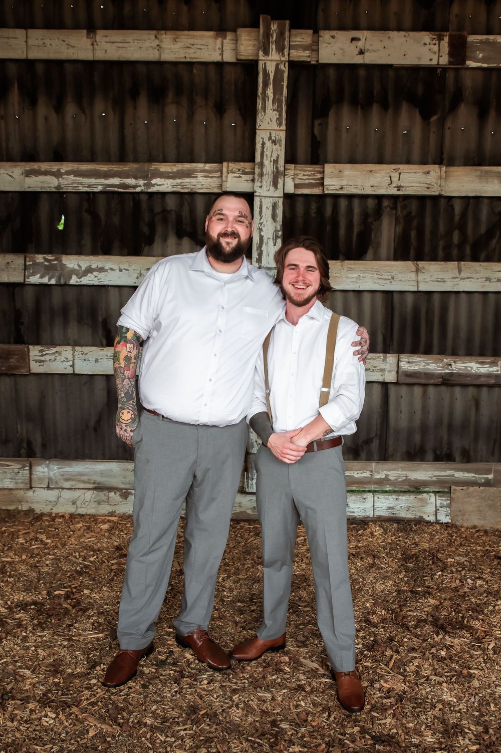 Two people in coordinated outfits share a laugh while posing in a rustic barn setting.