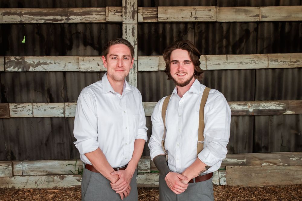 Two people in matching attire pose against weathered wooden barn walls.