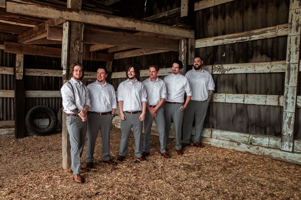 Group photo of wedding party members in coordinated gray and white attire inside rustic barn.