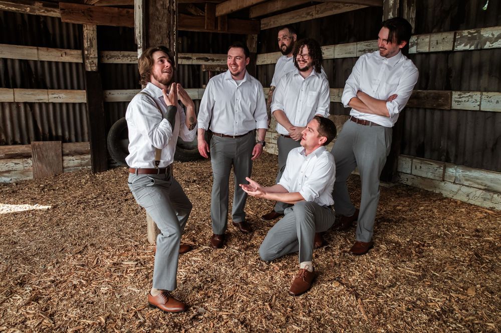 Wedding party members pose casually in matching outfits inside wooden barn structure.