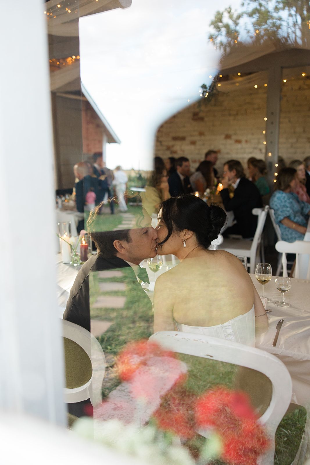 A couple shares a tender moment during their wedding reception in a rustic venue with string lights and floral decor.