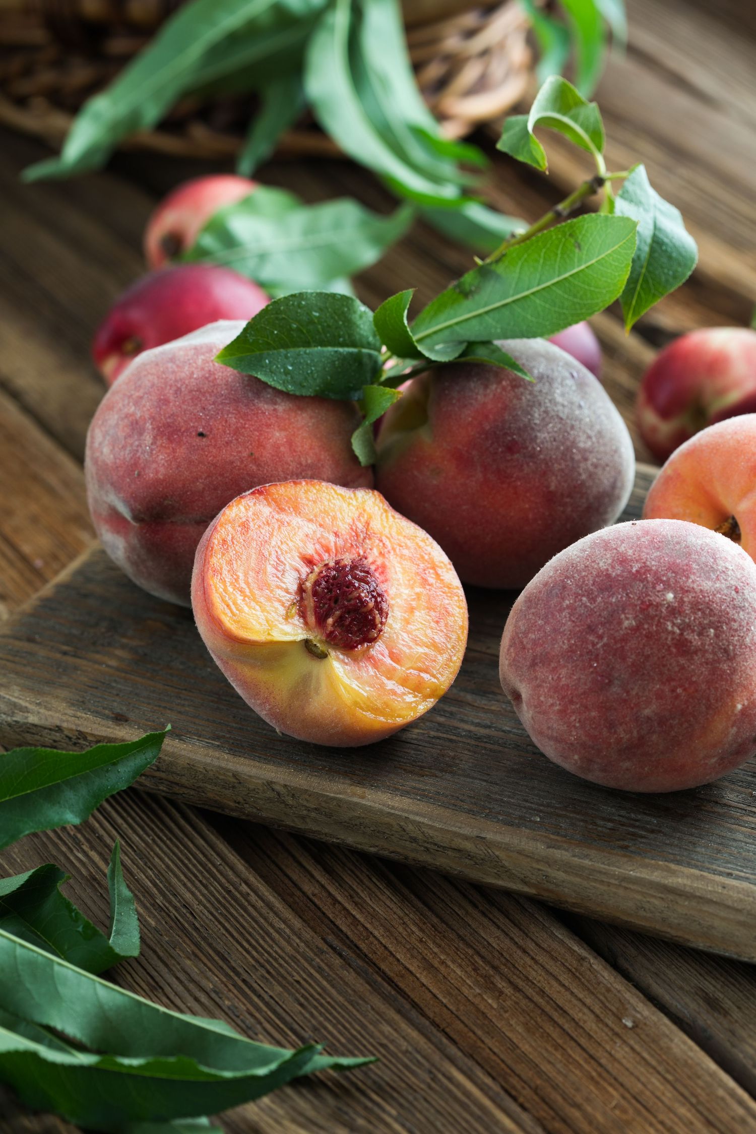 Fresh ripe peaches with green leaves arranged on rustic wooden board in natural lighting.