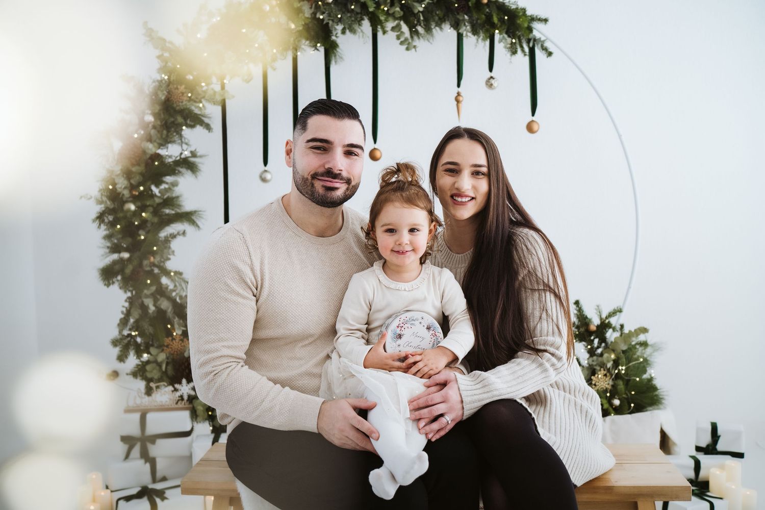 A family poses together in front of a white wall with hanging greenery and holiday decorations.