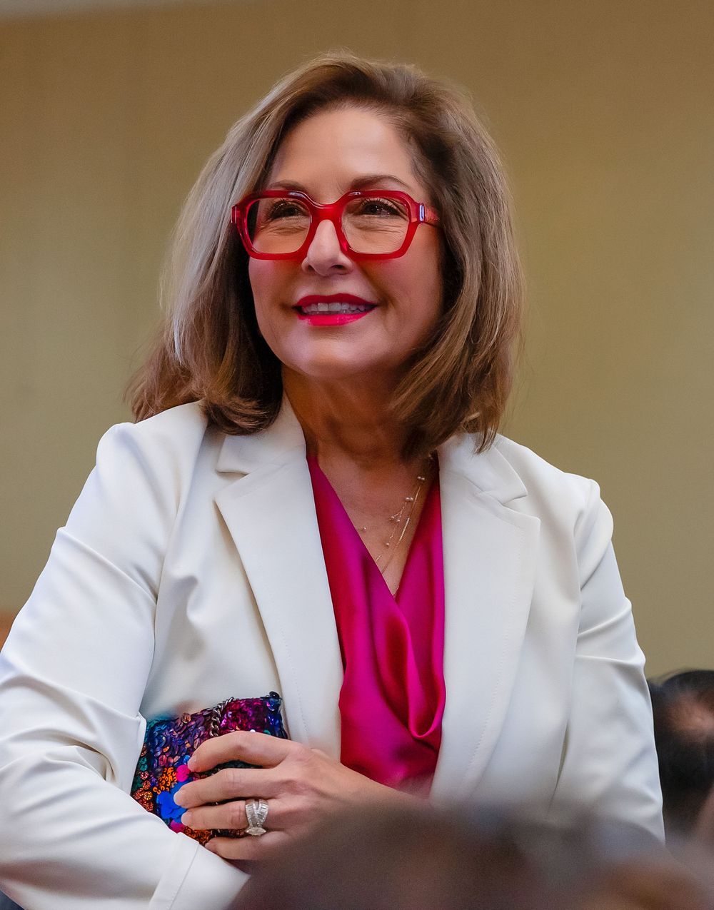Candid shot of woman in white jacket and pink shirt at an event session.