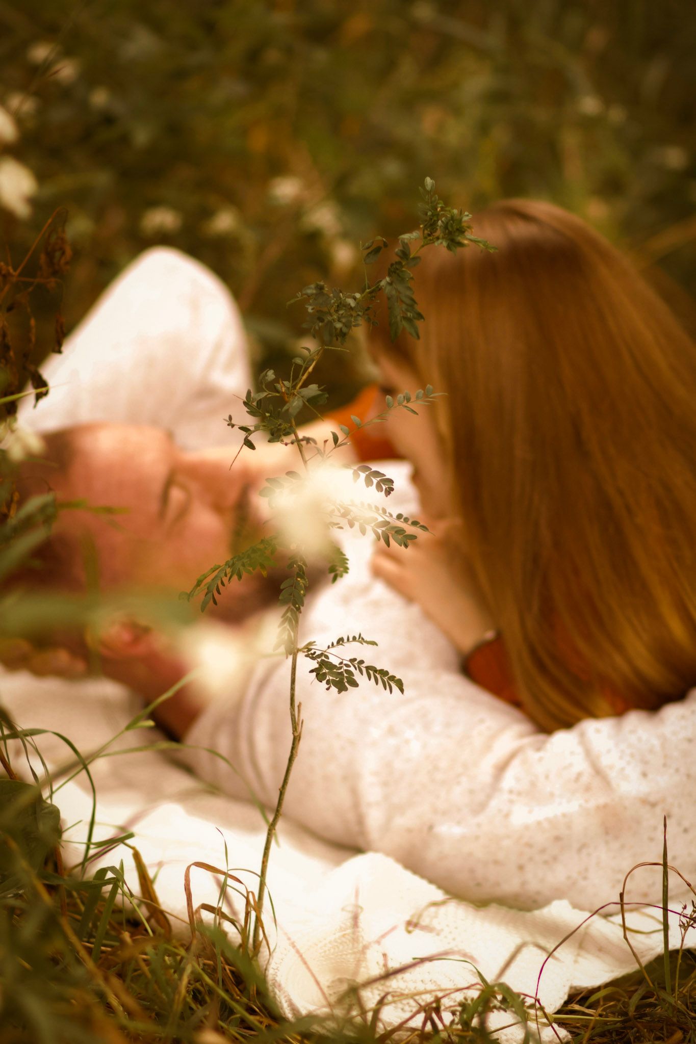 A couple lying in a meadow surrounded by delicate wildflowers at sunset.