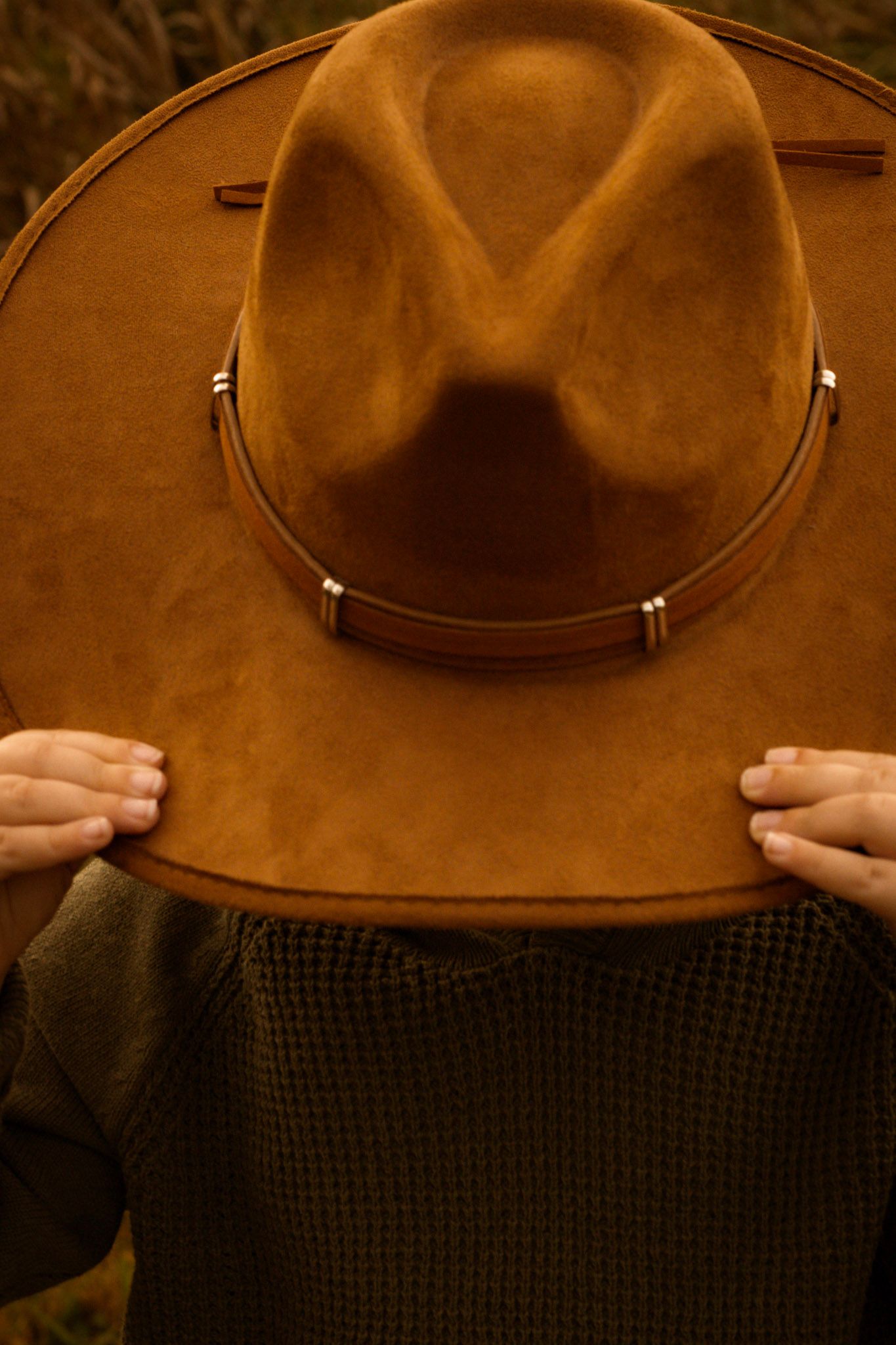 Close-up details of a brown leather cowboy hat against textured fabric.