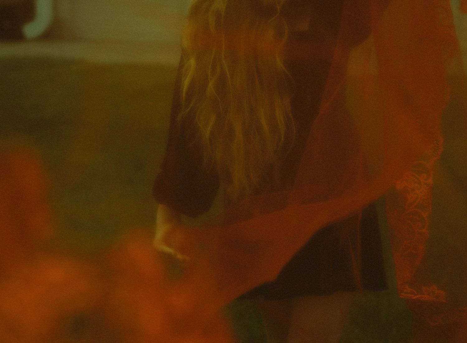 Blonde woman in orange and black outfit dancing in warm amber toned light indoors.