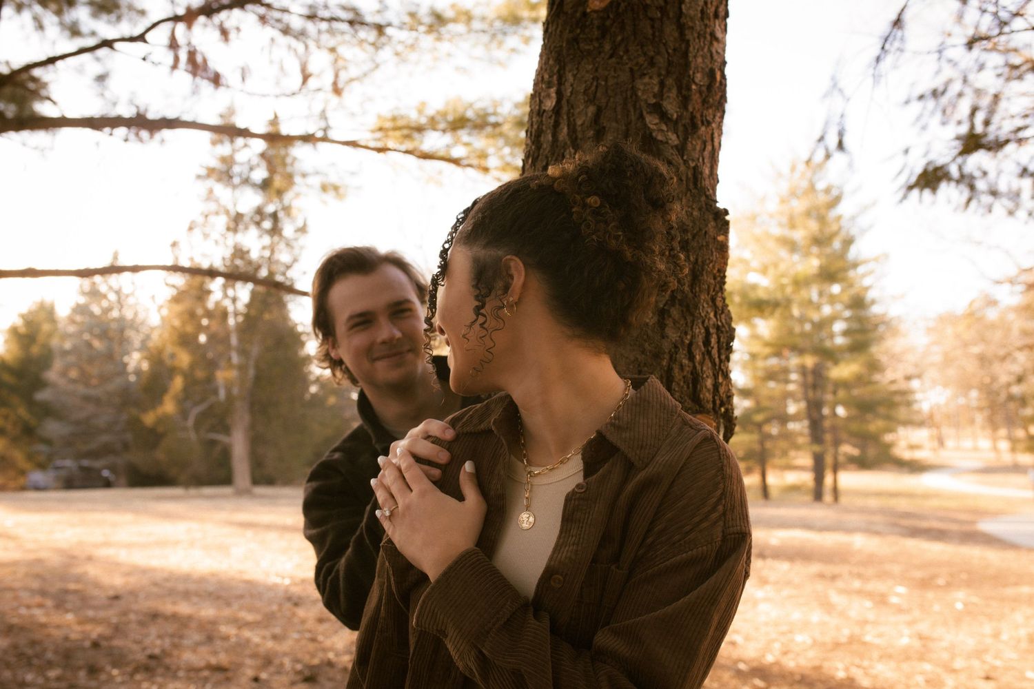 A couple shares an intimate moment in a golden-lit forest during an autumn engagement photoshoot.