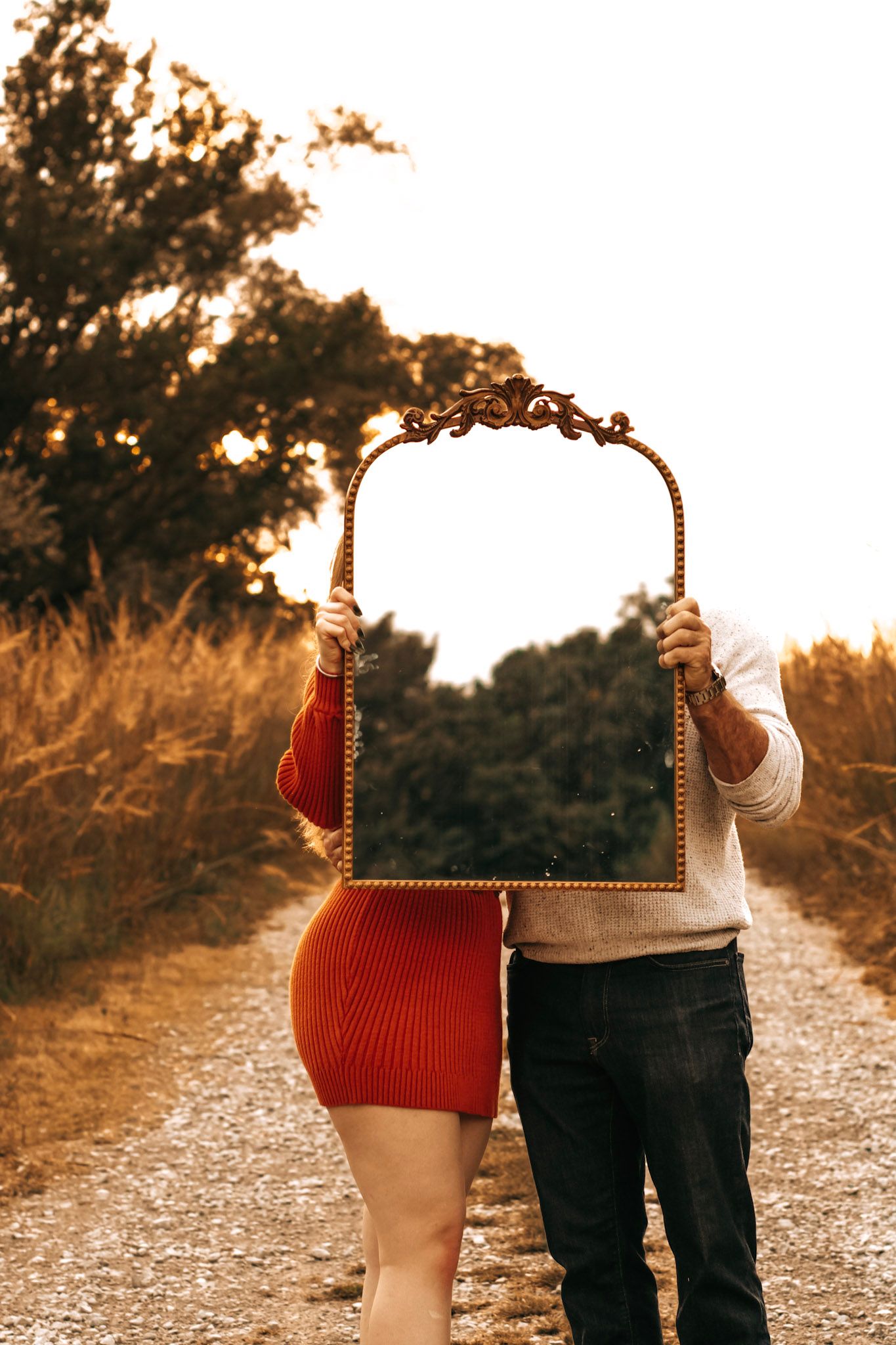 Two people walk hand in hand down a gravel path at sunset creating a romantic silhouette against warm golden light.
