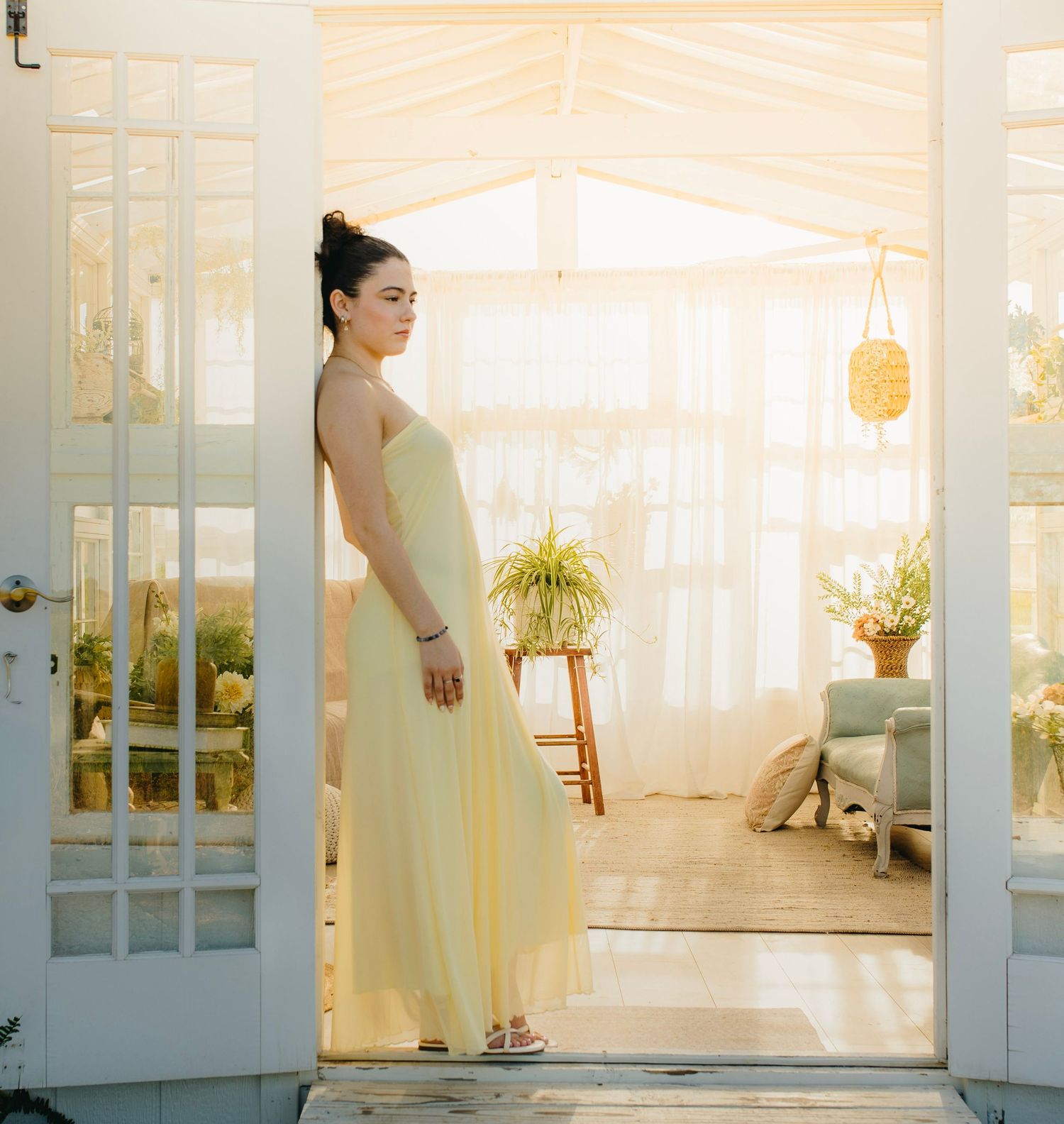 Bride in flowing yellow strapless gown standing in French doors of bright sunlit greenhouse space.