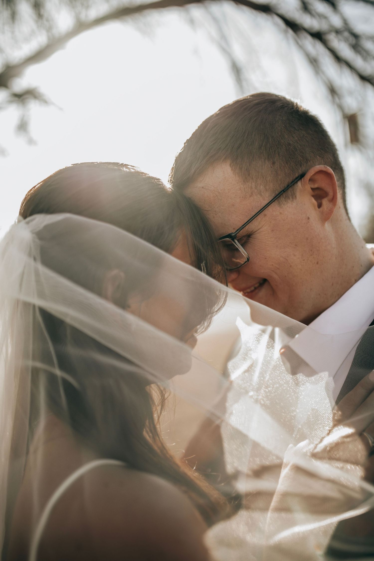 A romantic wedding moment captured in soft sunlight as a couple shares an intimate moment under a veil.