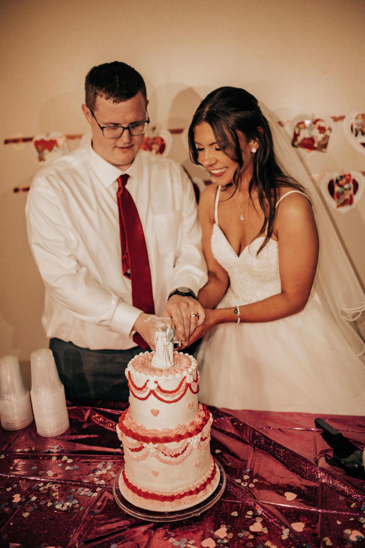 A couple shares a romantic moment while cutting their white and red wedding cake at their reception.