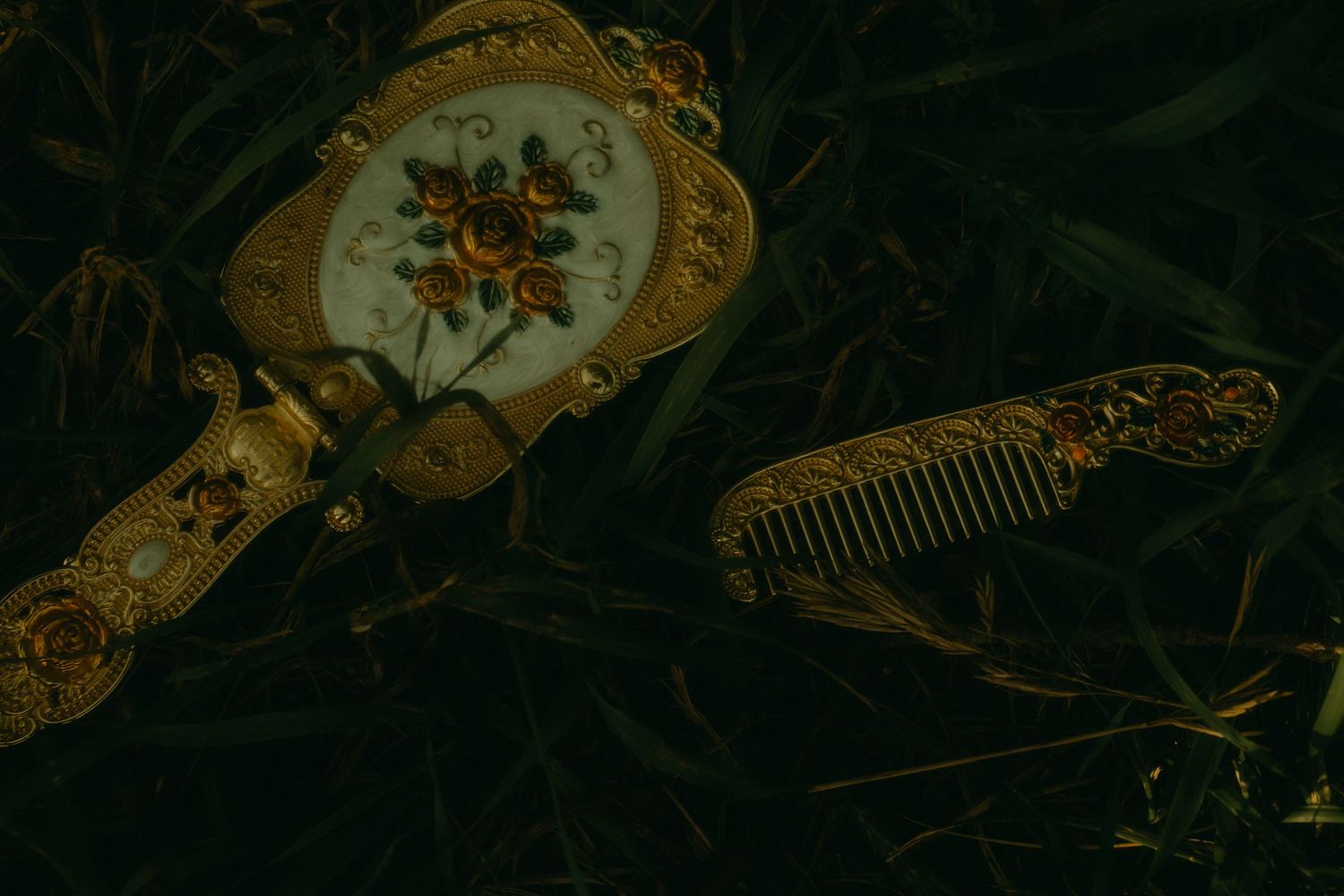 Vintage ornate golden hand mirror with floral design and matching comb resting on dark green foliage.