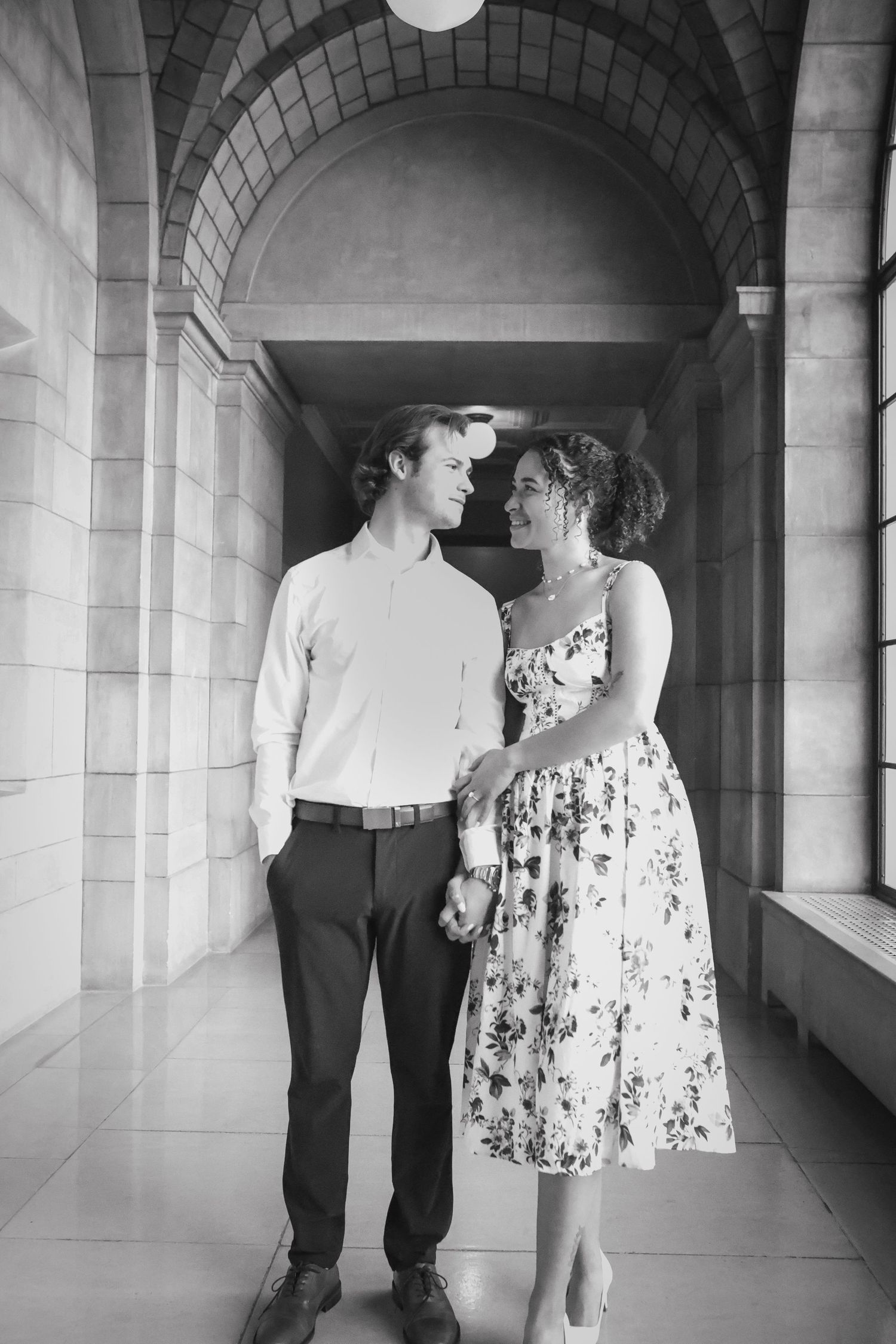 A black and white photo series showing a couple in a corridor with arched columns and stone architecture.