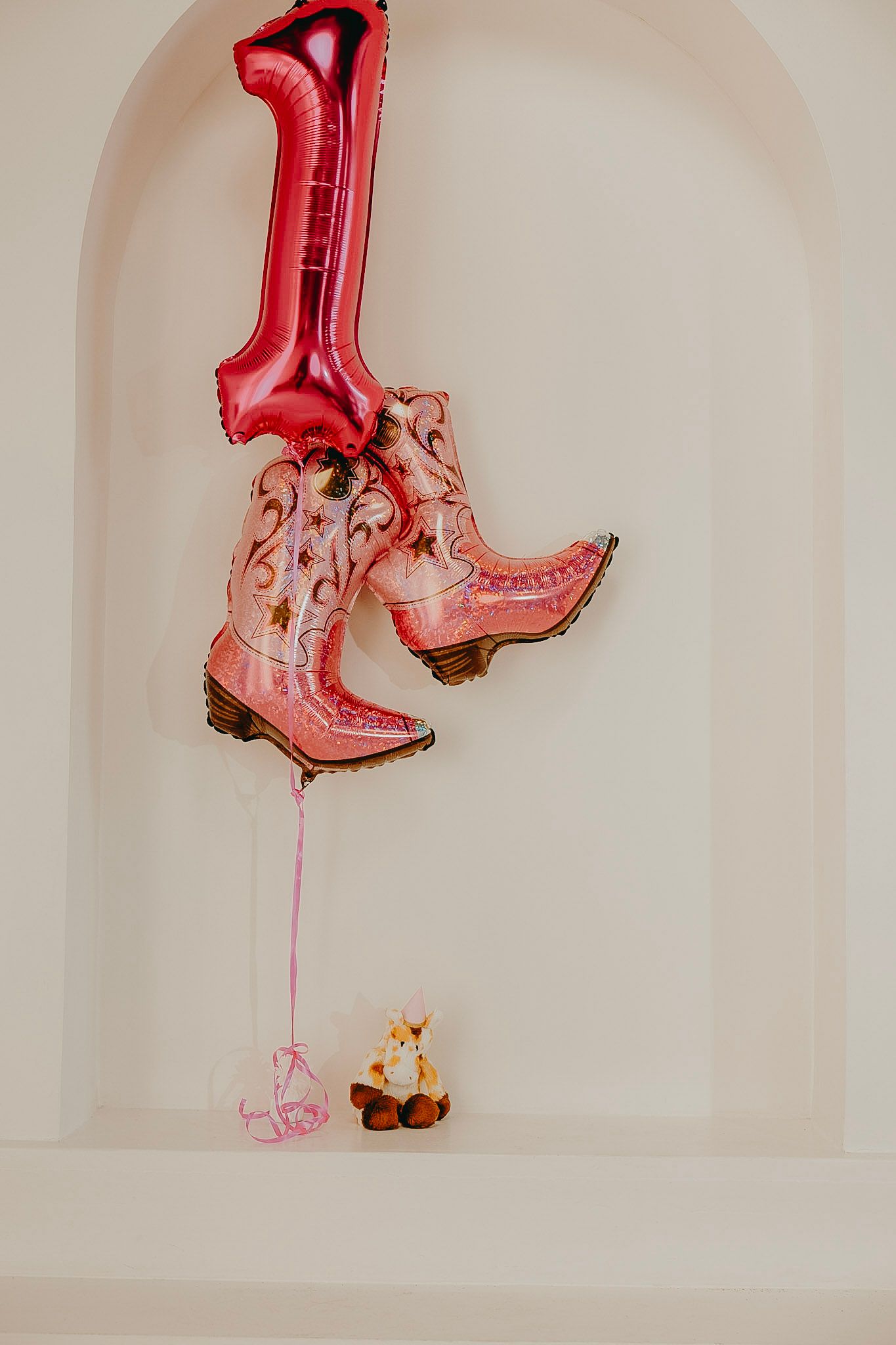 Pink cowboy boots and number 1 foil balloons with a small fox stuffed animal for a first birthday party.