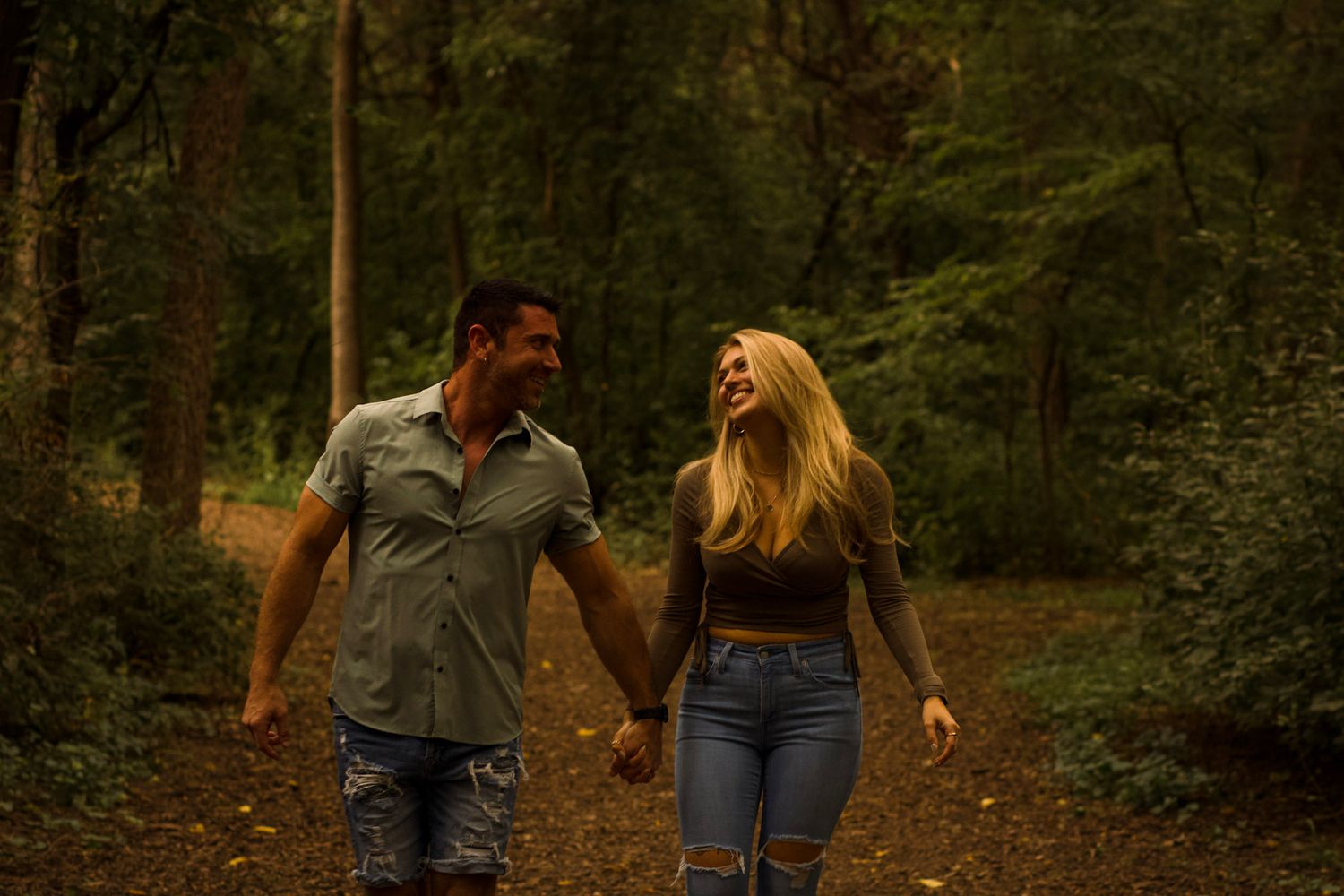 Two people stroll together on a tree-lined path at sunset.