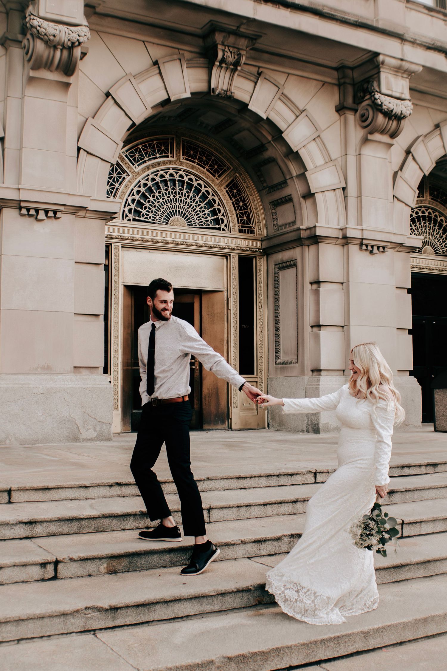 A couple dances playfully on grand stone steps of a historic building.