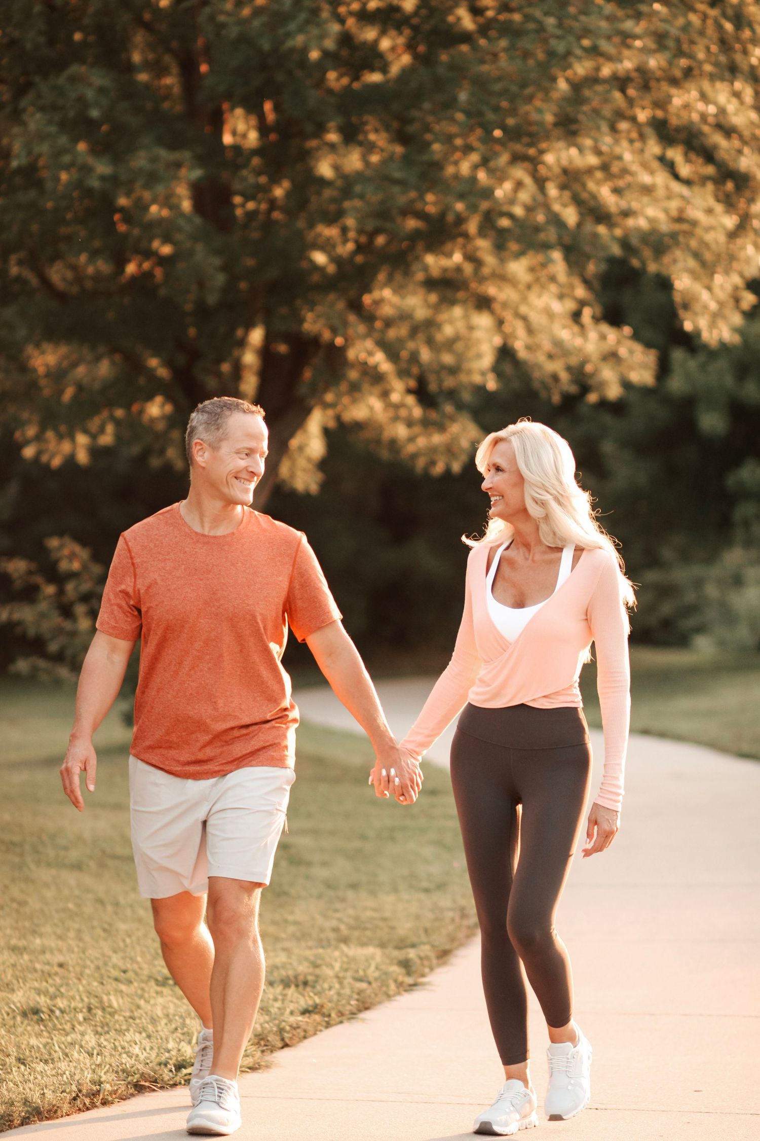 A couple jogs together on a sunlit path wearing coordinating orange and black athletic wear.