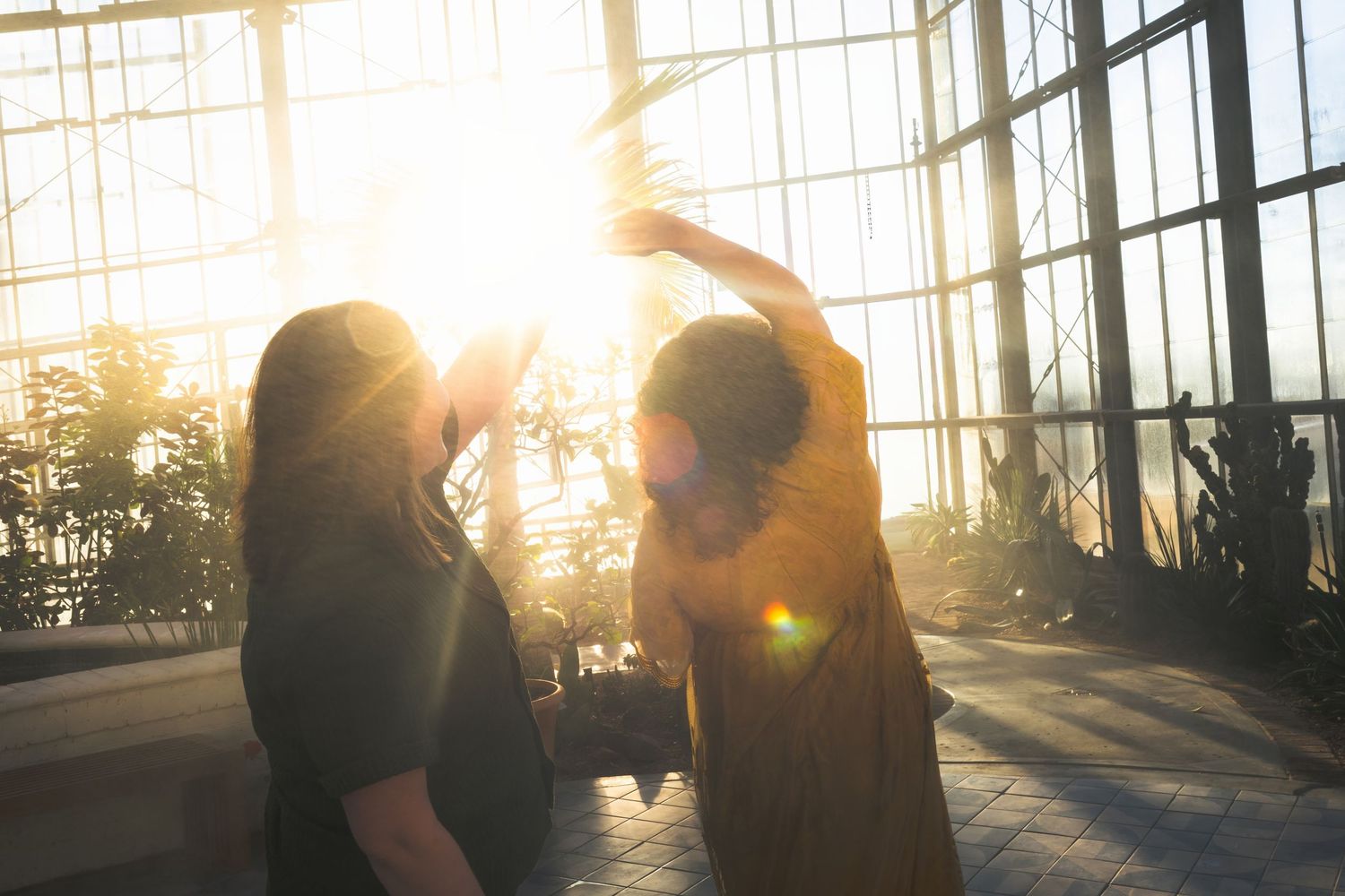 Silhouetted couple embraces against dramatic sunset through glass windows creating romantic backlit effect.