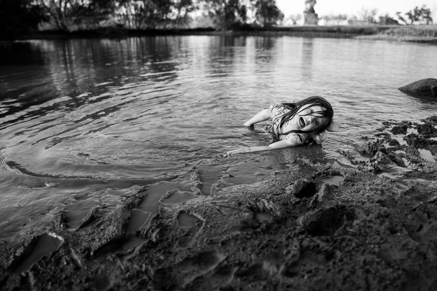 Tulsa photographer catches raw moment of a girl in  laying in muddy pond during family photography session